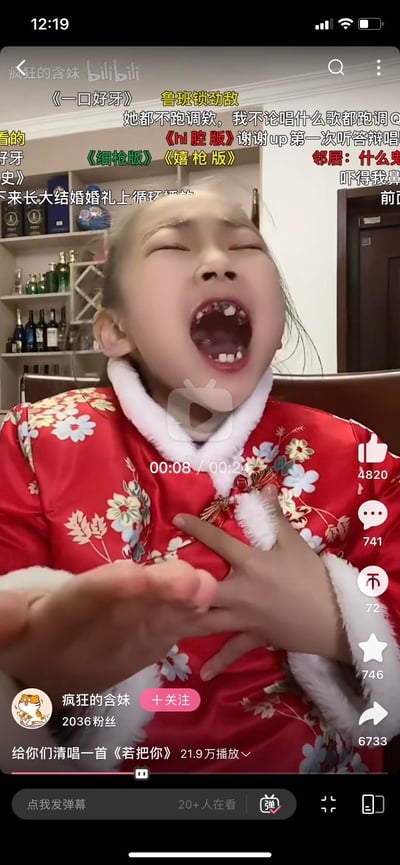 这是B站用户@疯狂的含妹发布的一段视频截图，画面中穿着红色中式花棉袄的小女孩张大嘴巴，以嘶吼的方式投入地清唱歌曲《若把你》，嘴里缺了好几颗牙的模样加上夸张的表情，搭配满屏的搞笑弹幕，显得十分魔性。弹幕内容包含《一口好牙》《鲁班锁劲敌》《hi腔版》等玩梗内容，还有网友调侃自己唱歌跑调、要在婚礼循环播放这段视频等，视频的互动数据亮眼，点赞4820、评论741、转发6733，整体氛围搞笑又充满欢乐感。