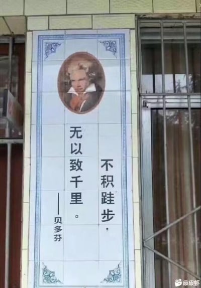 这是一幅张贴在建筑墙面上的瓷砖标语图，整体为竖版构图。画面上方是音乐家贝多芬的椭圆形肖像，肖像下方配写着“不积跬步，无以致千里。——贝多芬”的文字。但实际上“不积跬步，无以至千里”是中国古代思想家荀子《劝学》中的名句，并非贝多芬的言论，属于典型的张冠李戴乌龙，制造出荒诞的反差感，显得十分搞笑。