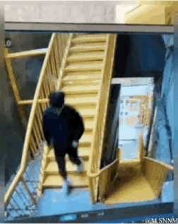这是一段整蛊类动态GIF，画面中一名身着黑色上衣的男子正走向一段黄色楼梯，当他行至楼梯中段时，才发现楼梯下半部分是绘制在地面的视觉错位图案，一脚踩空后失去平衡摔倒，意外又搞笑的场景充满了整蛊效果。
