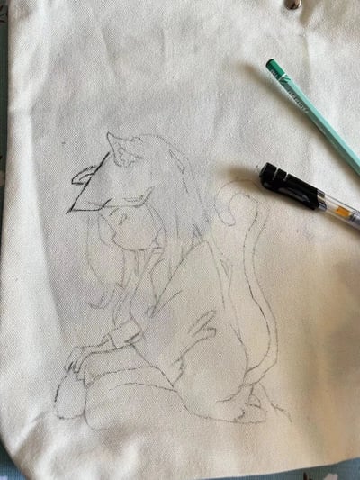 一张帆布纸上的手绘动物线稿，描绘了一个坐姿的动物角色，有着长长的耳朵和尾巴，线条简洁流畅。画面右侧放置了两支绘画工具：一支绿色铅笔和一支黑色马克笔，展现了绘画创作的场景。