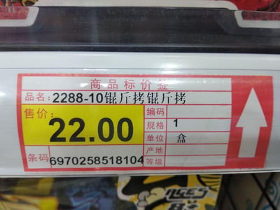 图片近距离拍摄了一张商品标价签，标签为红白色边框设计，顶部标注“商品标价签”字样。品名栏显示“2288-10锟斤拷锟斤拷”，存在明显的乱码问题；售价以黄色底纹突出显示为“22.00”元，右侧标注编码、规格（1盒）、单位、产地、等级等信息，底部有条形码“6970258518104”。乱码“锟斤拷”通常是由于文本编码错误（如GBK与UTF-8转换不当）导致的字符显示异常。