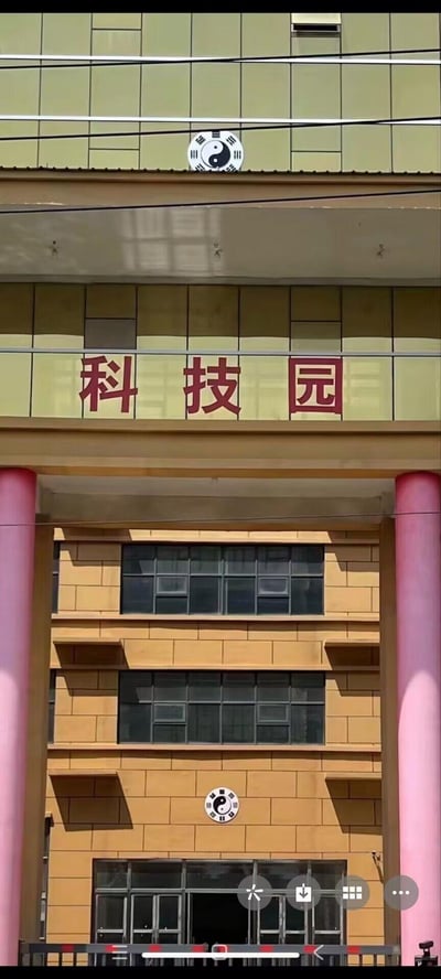 这是一张实拍的建筑入口照片，建筑中层位置有醒目的红色“科技园”字样，在字样的上方檐口处，以及建筑底层入口的墙面上，都设置了带有八卦符号的标识。现代科技园区的定位和传统玄学的八卦符号形成了有趣的反差感，让人觉得违和又好笑。