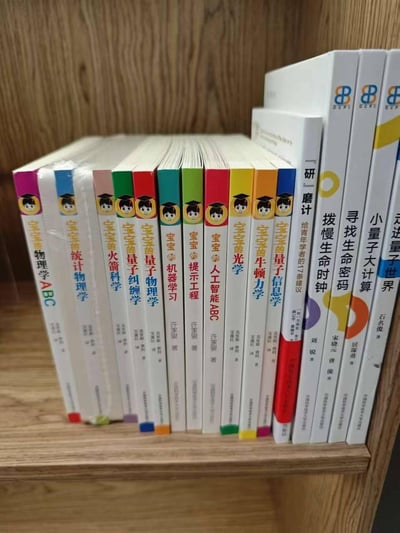 书架左侧整齐排列着10余本色彩鲜艳的儿童启蒙书籍，书脊印有戴学士帽的卡通婴儿形象，书名却极为硬核：从《宝宝量子力学ABC》《宝宝火箭科学》到《宝宝人工智能ABC》，涵盖量子纠缠、光学、牛顿力学等尖端科学领域。右侧则是成年人阅读的严肃书籍，包括《研一磨计》《拨慢生命时钟》《寻找生命密码》等，封面设计简约，标题聚焦现实议题。图片通过极端反差制造幽默效果，讽刺当下教育内卷中「从娃娃抓起」的荒诞现象——婴儿还在学ABC的阶段，却被赋予掌握量子物理的「重任」，对比成年人面对的实际生存压力，形成强烈的黑色幽默。