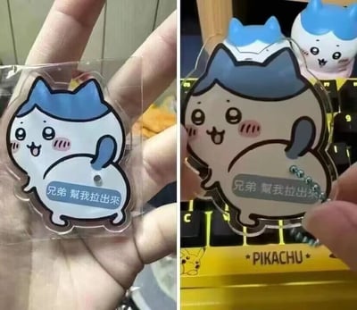 图片为左右对比图，左侧展示一只手握着透明亚克力材质的卡通猫咪吊坠，吊坠主体为蓝耳白猫形象，脸颊泛红，嘴巴张开呈开心状，腹部有文字“兄弟 帮我拉出来”；右侧展示同一吊坠被放置在带有Pikachu标志的键盘上，背景中还有另一个相似的蓝耳猫吊坠。整体风格可爱搞笑，突出商品的外观细节。