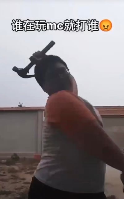 图中是一位戴眼镜的真人男性，手持扳手举过头顶，摆出要挥打的动作，画面上方配有文字“谁在玩mc就打谁😠”。这里的“mc”指沙盒游戏《我的世界（Minecraft）》，这张图是游戏圈的玩梗内容，以夸张的“愤怒”姿态调侃MC玩家，整体是戏谑搞笑的玩笑性质，并非真的带有恶意。