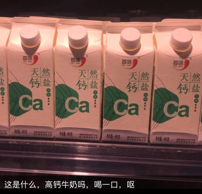 图中展示了超市货架上一排首味品牌的天然钙盐，其包装采用了类似高钙牛奶的利乐盒样式，醒目的“Ca”标识和“天然钙盐”字样容易让人混淆成牛奶。下方配文“这是什么，高钙牛奶吗，喝一口，呕”，模拟了误将钙盐当作牛奶饮用后的崩溃反应，用生活化的吐槽制造搞笑效果。