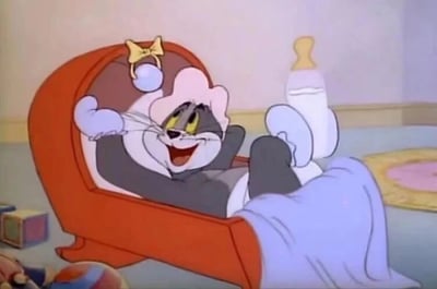 经典卡通《猫和老鼠》中的汤姆猫化身婴儿，戴着粉色婴儿帽，穿着白色婴儿鞋，舒适地躺在红色婴儿床里，双手枕在头后，双脚翘起，脸上洋溢着灿烂的笑容，显得十分开心和放松。床边放着一个大大的奶瓶，周围还有积木等婴儿玩具，营造出一种反差萌的搞笑效果。