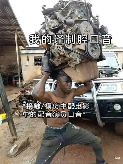 这是一张趣味梗图，以一名在简陋汽修厂内、赤裸上身吃力扛着沉重汽车发动机的非洲汽修工人的实拍照片为底图，搭配文字形成幽默效果。顶部文字“我的译制腔口音”将沉重的发动机类比为自身鲜明的译制腔口音，底部文字“*接触/模仿中配电影中的配音演员口音*”则解释了这种口音的来源，通过夸张的视觉反差，生动又搞笑地调侃了因模仿中配电影而形成译制腔口音的经历。