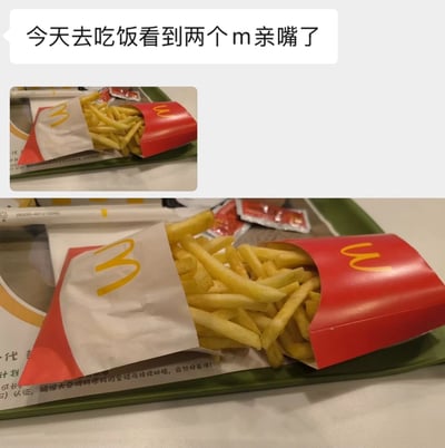 图片上方有一个白色对话气泡，内容为“今天去吃饭看到两个m亲嘴了”。下方是两张麦当劳薯条盒的照片：小图展示两个红色薯条盒放在绿色托盘上，黄色M标靠近；大图特写两个薯条盒的M标紧密接触，视觉上形成“亲嘴”的趣味效果。这是一个利用麦当劳标志性M logo进行的创意联想，通过物品摆放制造出拟人化的搞笑场景。
