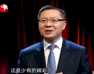 这是一张东方卫视政论节目《这就是中国》的视频截图，画面主体是学者张维为，他身着深色西装、白色衬衫，搭配蓝色花纹领带，戴着眼镜，面带微笑，正处于发言状态，似乎在对某事物给出正面评价。画面底部配有白色字幕‘这是少有的精彩’，背景是暗红色的幕布，左上角有东方卫视的红色五角星台标，整体构图清晰，是典型的节目录制场景。