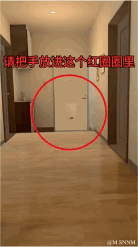 这是一个利用视觉错位原理制作的动态GIF图，画面展示了一段室内走廊，远处的门被红色圆圈标注，同时配有文字“请把手放进这个红圈圈里”。利用近大远小的视觉错觉，让观看者产生可以将手放入圈中的错觉，是一个趣味整蛊类的视觉小把戏，用来制造轻松搞笑的效果。