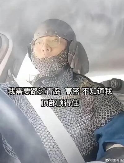 图中是一位坐在汽车驾驶座上的真人，身着中世纪风格的锁子甲与头盔，系着汽车安全带，画面充满复古装备与现代出行场景的反差感。图中配文“我需要路过青岛 高密 不知道我顶部顶得住”包含双关梗：“顶部”一方面指头上的头盔，另一方面谐音“顶不顶得住”的“顶”，用硬核装备调侃路过两地时的莫名担忧，风格荒诞又搞笑。
