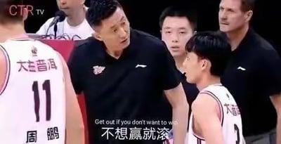 篮球比赛期间，一位穿着黑色上衣的教练正对身穿白色球衣的球员发怒训斥，周围有其他球员和工作人员围观。教练神情愤怒，指向球员，图中叠加文字显示其训斥内容：“不想赢就滚”，并配有英文翻译“Get out if you don't want to win”。球员球衣胸前印有“大益普洱”字样，其中一名球员背后印有姓名“周鹏”及号码“11”。