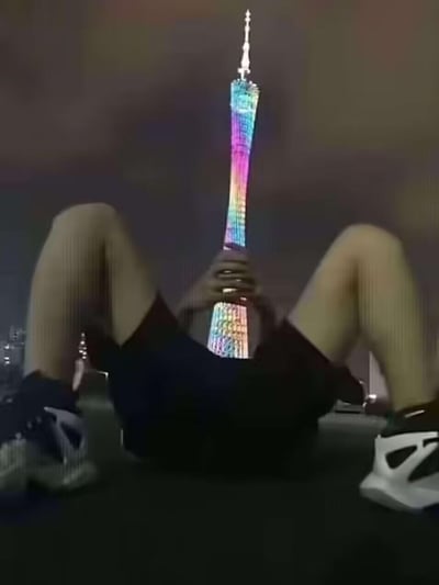 这是一张利用视觉错位拍摄的趣味图片，画面中真人平躺，双腿弯曲分开，双手在身前交叠，背景的广州塔（小蛮腰）恰好处于人物双腿与双手之间的位置，从拍摄角度看，仿佛是人物“握着”广州塔，制造出荒诞又搞笑的视觉错觉，创意十足。