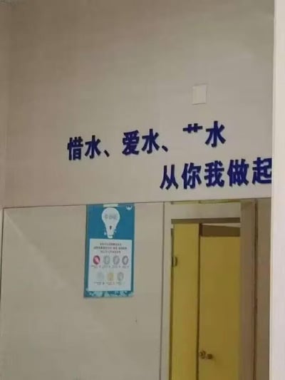 这是一张室内公共场所的实拍竖图，墙面上方张贴着蓝色的节水宣传标语，内容为“惜水、爱水、**水 从你我做起**”，其中第三个与“水”搭配的核心词汇被两个星号打码遮挡，留下悬念。标语下方的墙面上贴有一张蓝白配色的节能主题海报，海报带有灯泡图案和若干图标文字。画面右侧可见一扇黄色的房门，整体场景推测是办公楼、学校或公共场馆等需要倡导节水节能的内部区域。