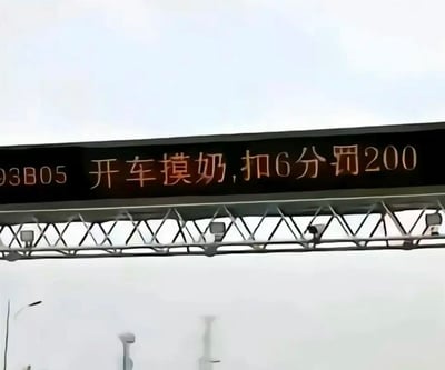 图片展示了一个道路 overhead 交通指示牌，牌面显示红色文字“开车摸奶,扣6分罚200”及编号“93B05”。背景为灰白色天空，标语牌由金属三角支架支撑，整体呈现出道路监控或提示牌的典型结构。内容中“摸奶”一词属于低俗表述，明显不符合正规交通标语规范，推测为恶搞或P图修改的娱乐性内容。