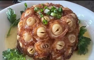 图片展示了一道传统中式菜肴，主体为圆形分层结构的扣肉，每层面肉中间嵌有一颗完整栗子，肉质呈现棕红色，表面油亮。顶部点缀着翠绿的葱花，周围摆放着新鲜香菜叶，底部有淡黄色酱汁浸润，整体盛放在白色瓷盘中。菜品造型精致，层次分明，色彩搭配鲜明，展现出中式烹饪的匠心和美感。