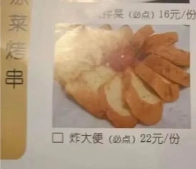 这是一张餐馆菜单的实拍图，左侧竖排标注分类为“凉菜烤串”，图中展示了两道标注为必点的菜品，上方菜品文字模糊，显示售价16元每份；下方菜品配有实拍图，是摆成花瓣形状的切片炸物，对应的菜品名却标注为“炸大便”，售价22元每份，明显为菜单输入时的错别字，该离谱的错误极具喜剧效果。