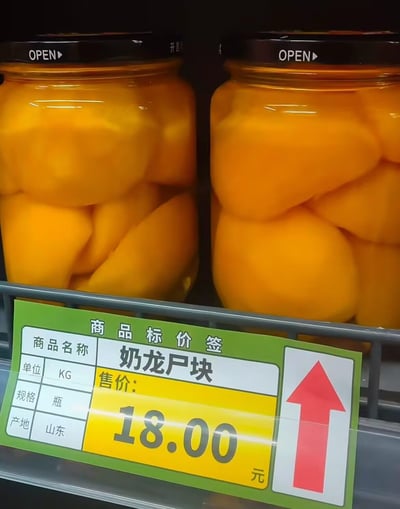 这张图片拍摄于超市，画面中有几瓶罐头黄桃，下面的商品价格标签却写着“奶龙户块”，让人哭笑不得。明明是常见的水果罐头，却因标签错误成了莫名其妙的新梗，产生了幽默和荒诞感。在中文网络语境中，这样的乌龙标签图常常用来自嘲生活小槽点。**“奶龙户块”不是实际商品名，纯属标签贴错或者打印机乌龙造成的笑点。**