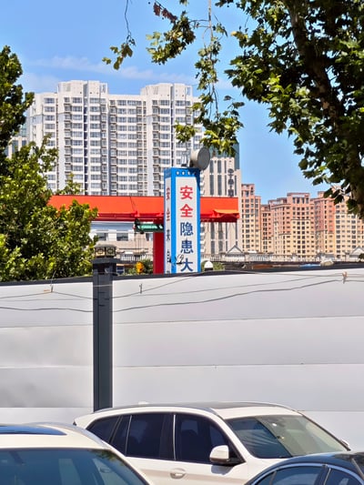 图片拍摄于一处城市工地外，前景有多辆私家车，背景则是高层住宅和仿古建筑。工地围挡上方竖立着蓝白色的警示标志，垂直写着“安全隐患大”。这一标语本意应为“安全隐患大排查”之类，但因排版问题和断句角度，读起来变成“安全隐患大”，意指“这里隐患很大”，形成幽默反差，属于典型的低级翻车现场。并体现了网络常见的“断句梗”。

双关/梗点：因为排版和视角误导，使强调安全的标语变成反向暗示工地很危险，形成幽默效果，被网友频繁二次创作和调侃。