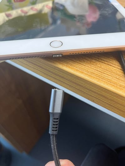 这张图片展示了一台带有Touch ID的金色iPad的底部区域，其Lightning充电接口内部的金属针脚已经出现变形、损坏的情况；下方被手持的Type-C转Lightning转接线的公头也同样出现针脚断裂、弯折的损坏状态，推测是插拔过程中操作不当导致接口与接头双双损坏。
无谐音梗、双关或暗示内容。