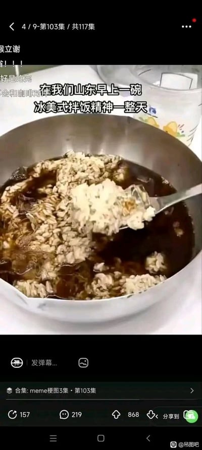 图片展示了一碗装有米饭和深色液体（疑似酱油或咖啡）的不锈钢碗，勺子正从碗中舀起拌有液体的米饭。画面上方配有文字“在我们山东早上一碗冰美式拌饭精神一整天”，以幽默夸张的方式调侃山东特色早餐，营造出轻松搞笑的氛围。