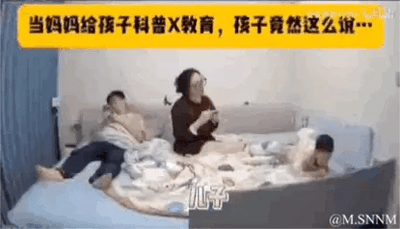 这是一段家庭日常的视频截图，场景在卧室的床上：妈妈坐在床中间，似乎正在给孩子科普性教育相关内容；左侧的大儿子裹着被子靠在床头，表情看起来有些害羞或尴尬；右侧的小儿子趴在床上，好奇地看向妈妈。画面上方的黄色标题栏写着“当妈妈给孩子科普X教育，孩子竟然这么说…”，下方标注“儿子”的字幕，暗示孩子接下来的回答会出人意料，制造出搞笑的反差感，展现了亲子间有趣的互动瞬间。