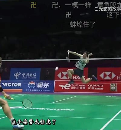 这是一张羽毛球国际赛事的视频截图，画面中一名男选手腾空跃起准备击球，身体与手臂的姿态恰好组成了类似‘卍’的形状，引发网友玩梗。画面上方添加了‘卍，一模一样’‘蚌埠住了’等调侃弹幕，画面底部配有字幕‘这个姿势太标志了’，整体氛围趣味搞笑，是网友对体育赛事画面的二次创作玩梗。
无特殊双关、谐音梗或暗示，单纯以选手的巧合姿势进行趣味调侃。