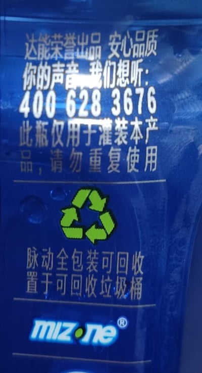这是一张脉动（mizone）饮料瓶身下部的实拍图，背景为深蓝色的瓶身材质，上面印有金色、白色的文字与标识。内容分为多个板块：顶部是'达能荣誉出品 安心品质'的品牌背书，接着是消费者反馈热线'你的声音 我们想听：400 628 3676'；随后是使用提示'此瓶仅用于灌装本产品，请勿重复使用'；再往下是环保回收指引，配有绿色的可回收标志，文字为'脉动全包装可回收 置于可回收垃圾桶'；最底部是脉动的英文品牌标识'mizone®'。整体排版规整，信息清晰，是产品包装的标准官方说明内容，无谐音梗、双关或暗示类内容。