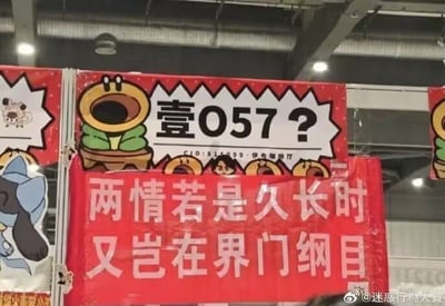 室内活动场景中悬挂的创意横幅，上方横幅以红色为底，配有向日葵卡通形象和文字“壹057?”及“CID:815193 - 伊布聯盟”；下方红色横幅则改编经典诗句“两情若是久长时，又岂在朝朝暮暮”为“两情若是久长时 又岂在界门纲目”，将“朝朝暮暮”替换为生物学分类术语“界门纲目”，形成幽默的跨学科梗，展现活动的创意与趣味性。左侧还可见蓝色伊布（宝可梦角色）及小狗卡通形象。