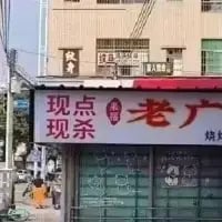 这是一张街头餐饮店铺的实拍照片，画面主体是一家烧腊店的招牌，招牌上以醒目的字体写着“现点现杀”和“老广”，右下角标注有“烧腊”字样，背景是一栋居民楼，充满了市井生活的烟火气，直观展示了这家主打新鲜现做的广式烧腊店的特色。