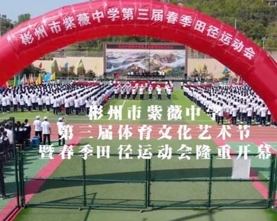 图片展示了彬州市紫薇中学第三届春季田径运动会的开幕式现场。画面中央是巨大的红色充气拱门，上面写有“彬州市紫薇中学第三届春季田径运动会”字样。拱门下方，数百名身着白色校服的学生整齐列队，形成有序的方阵。背景中可见搭建的主席台，上方有山水图案的背景板，两侧插着各色旗帜，整体场面庄重而热烈。图片中央叠加文字“彬州市紫薇中学 第三届体育文化艺术节 暨春季田径运动会隆重开幕”，明确了活动主题。