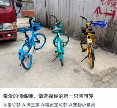 画面展示了三辆停放在水泥地面的共享单车，从左至右分别是蓝色哈啰单车、青绿色青桔单车、黄色美团单车，背景可见红色卡车与带有高压电缆警示标语的铁皮围墙。图片下方配有文字：“亲爱的训练师，请选择你的第一只宝可梦”，并附带#宝可梦 #御三家 #精灵宝可梦 #宠物小精灵 话题标签。该图玩了宝可梦系列的经典梗，将三款主流共享单车对应宝可梦开局的初始御三家精灵，把日常出行工具代入ACG经典场景，制造出趣味的代入感与反差萌。