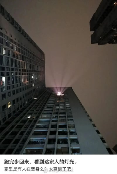 这是一张夜晚从低角度仰拍的高层居民楼照片，画面中几栋住宅楼在夜色里矗立，多数窗口透出零星灯光，其中一栋楼的顶部窗口透出的灯光向四周呈放射状散开，视觉效果酷似特摄影视作品里角色变身时的标志性特效光束。图片下方配有调侃的文字：“跑完步回来，看到这家人的灯光。家里是有人在变身么？太离谱了吧！”，用幽默的语气吐槽这个巧合的趣味场景，让普通的生活画面充满了二次元的脑洞感。