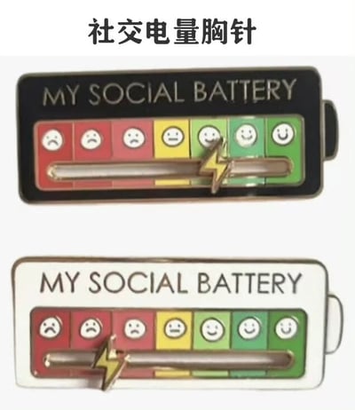图片展示了两款名为“社交电量胸针”的创意配饰，上下排列呈现。胸针整体设计为电池形状，上方黑色款和下方白色款均印有英文“MY SOCIAL BATTERY”字样。电池内部从左至右分为红、黄、绿三色区域，对应不同社交电量状态：红色区域（左三格）为悲伤表情😔，黄色区域（中间一格）为中性表情😐，绿色区域（右三格）为微笑表情😊。电池中间有一个带闪电符号的滑块指针，可手动调节至不同区域，直观展示佩戴者当前的“社交电量”——即社交精力状态，创意地将内向者/外向者的社交疲劳程度转化为可视化的“电池电量”隐喻。
