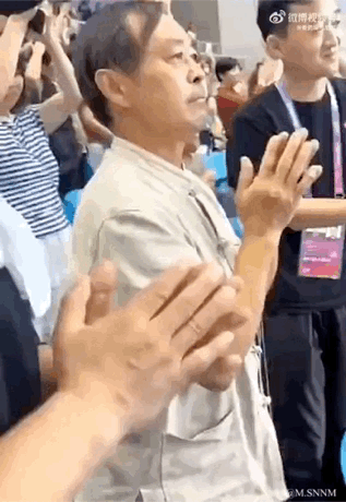 这是一段动态GIF内容，画面中演员张铁林身处活动现场的人群里，正抬手做出鼓掌动作，前景处有另一双手快速重复鼓掌动作，由于视觉错位的效果，看起来仿佛是张铁林的手在以超快频率鼓掌，制造出滑稽搞笑的视觉反差，常被用来表达热烈支持、起哄捧场的搞笑情绪。