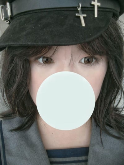 这是一张竖屏自拍照片，图中女生头戴带有金属十字装饰的黑色复古帽，留着深色碎刘海卷发，浅棕色的眼睛直视镜头，下半张脸被白色圆形遮挡。她身着灰色外套，内搭深色条纹上衣，整体风格偏向暗黑哥特风，气质清冷神秘。