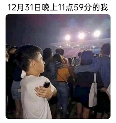 这是一张用来调侃跨年夜单身状态的搞笑梗图，图片上方配有文字“12月31日晚上11点59分的我”。画面呈现的是一个夜晚的户外人群场景，周围都是成对相拥的情侣，只有画面左侧的男生独自双臂环抱着自己，手里还拿着手机，神情落寞又无奈，和周围情侣的甜蜜形成强烈反差，精准戳中了跨年夜里单身人士的孤独处境，用这种反差感制造出搞笑又扎心的效果，引发单身群体的共鸣。