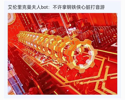 这是一张央视春晚鼓乐表演《鼓韵龙腾》的舞台截图，舞台上的齿轮状鼓组装置搭配红金配色的科技风舞台，整体造型高度神似漫威角色钢铁侠胸口的方舟反应炉。网友玩梗配文“不许拿钢铁侠心脏打音游”，将表演者打鼓的动作调侃成在游玩音游，利用造型相似性制造出搞笑的脑洞效果，把春晚舞台和漫威IP、音游元素结合，充满趣味。