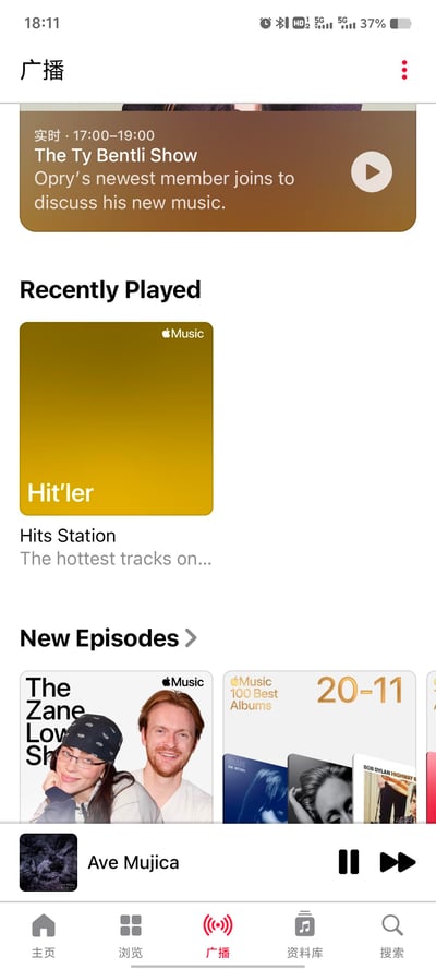 这是一张经过修改的Apple Music应用广播页面截图，界面顶部展示了实时节目《The Ty Bentli Show》的信息，标注播出时间为17:00-19:00，内容为邀请Opry新成员讨论新音乐。在“最近播放”板块中，出现了名为“Hit’ler”的热门电台，此处是玩谐音梗，将“Hitler（希特勒）”拆分为Hit’ler，伪装成正常的热门电台名称，制造出恶趣味的恶搞效果。界面下方“新剧集”板块展示了《The Zane Lowe Show》的宣传图以及Apple Music百佳专辑的内容，底部显示正在播放Ave Mujica的内容，导航栏处于“广播”选项。
**谐音梗说明**：将“Hitler”拆分为Hit’ler，伪装成“Hits Station”类的热门电台名称，属于恶趣味恶搞。