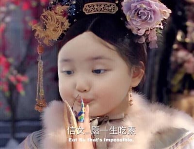 图片中是一位穿着古装、头戴华丽头饰（含金色龙形装饰和紫色花朵）的人物，双手合十似在祈福，面部表情认真。下方配有文字'信女愿一生吃素'及英文翻译'Eat Su that's impossible.'，源自《甄嬛传》经典场景改编的网络梗，表达年轻人'想许愿却不愿付出代价'的自嘲心理。