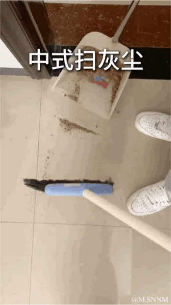 这是一个搞笑GIF，图中展示了一个人在扫地时的错误操作：拿着扫帚在地面扫动，但是簸箕却悬在门边上，完全没有对准要扫的灰尘，灰尘被扫到簸箕下方的地面，根本无法被扫进簸箕里。图上方配文“中式扫灰尘”，用反讽的方式调侃这种无效的打扫行为，充满了搞笑的反差感。
