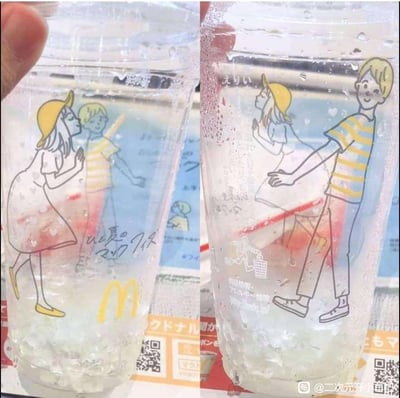 这是麦当劳推出的夏日限定冷饮杯，通过左右两张图展示杯子在满杯和空杯状态下的不同卡通场景：<br>1. 满杯时，戴黄帽的女生凑近条纹上衣男生，做出羞涩的索吻姿态；<br>2. 空杯时，男生转身朝向女生，形成双向奔赴的互动画面。<br>这个设计巧妙利用杯子的液体高度变化，遮挡或露出图案的不同部分，制造出充满夏日恋爱感的趣味场景，创意十足。