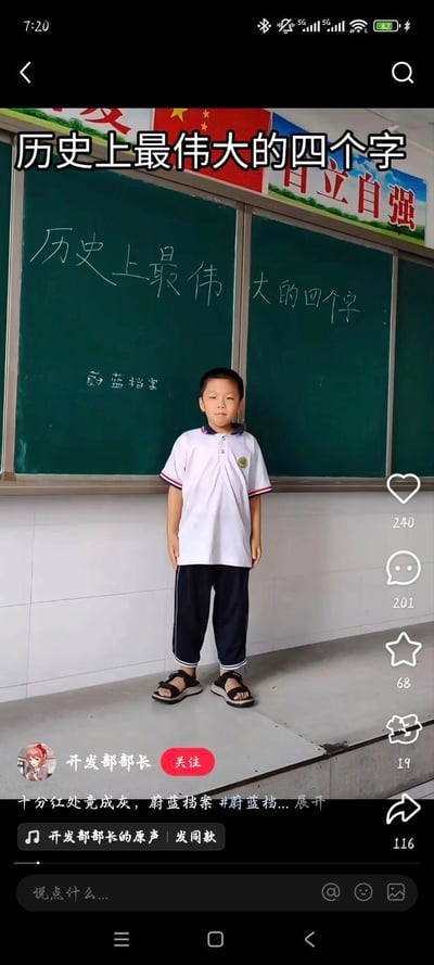 这是一张抖音短视频的竖屏截图，画面中一名穿着白色校服的小男孩站在教室的黑板前，黑板上用粉笔写着‘历史上最伟大的四个字’和‘蔚蓝档案’，视频顶部也叠加了同样的文字‘历史上最伟大的四个字’。这是一个玩梗内容，将游戏《蔚蓝档案》调侃为‘历史上最伟大的四个字’，用校园场景来制造反差感，达到搞笑调侃的效果。