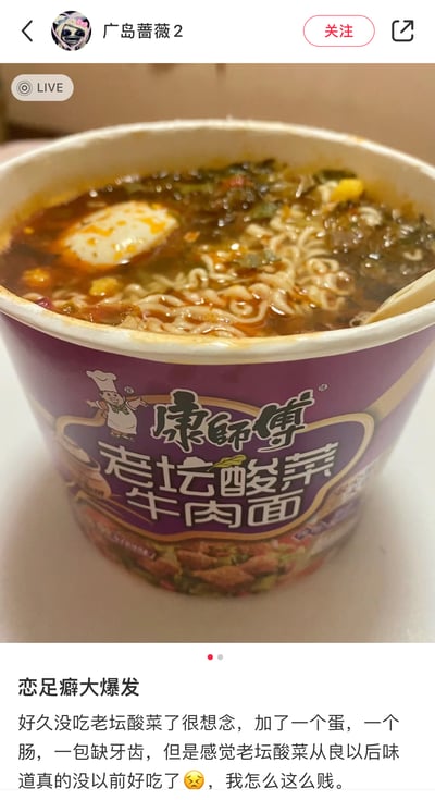这是社交平台用户「广岛蔷薇2」的直播截图搭配个人吐槽帖子，图中是泡好的康师傅老坛酸菜牛肉面，额外添加了卤蛋、肠和其他配料，汤汁浓郁。配文表示自己好久没吃这款泡面十分想念，加料食用后却觉得整改（自嘲为「从良」）后的老坛酸菜面味道不如从前，最后自嘲「我怎么这么贱」，尽显对旧版味道的怀念和对新版的小失望。