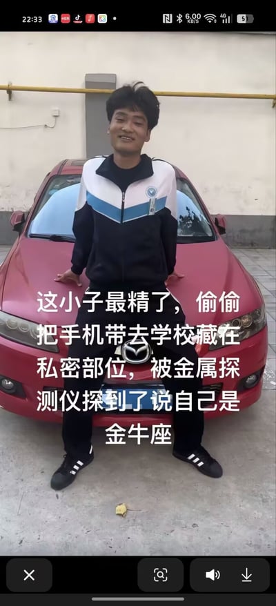 图片中一名穿着黑白蓝相间运动服的年轻男子站在红色轿车前，双手背在身后，面带微笑。图片上叠加文字讲述了一个搞笑故事：学生偷偷把手机藏在私密部位带进学校，被金属探测仪检测到时，机智地谎称自己是金牛座来掩饰。

这张图使用了谐音梗：金牛座（Taurus zodiac sign）的发音与“金属”相似，形成了幽默效果。