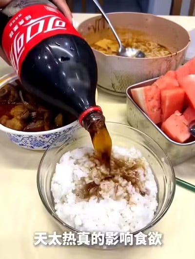 画面中一只手正将大瓶可口可乐倾倒在一碗白米饭上，周围的桌面上摆放着炖菜、汤品和切好的西瓜块，画面底部配有文字‘天太热真的影响食欲’，展现出因天气炎热食欲不佳，尝试用可乐泡饭这种新奇吃法的生活场景，没有双关、谐音梗或暗示内容。