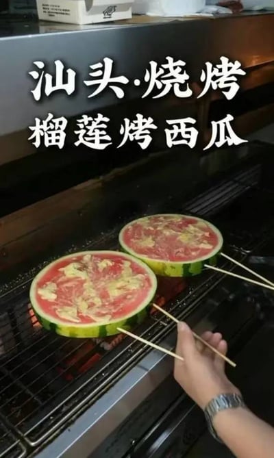 这张图片拍摄于烧烤摊，画面中用铁签插着切片圆形的西瓜放在炭火上烤制。西瓜表面融合了食材的自然红黄配色，非常吸引眼球。上方配有“汕头·烧烤 椰莲烤西瓜”大号白字，极具网络梗图风格，凸显奇葩美食创意。该画面常被网友用于调侃、吐槽新奇烧烤方式或猎奇美食创意场景。