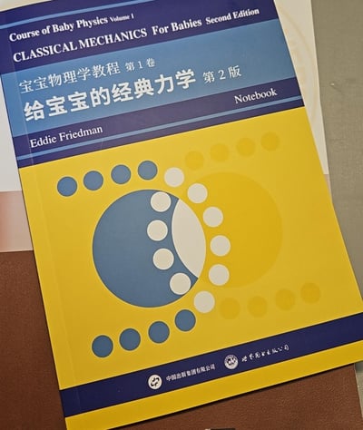 这是一本《宝宝物理学教程 第1卷 给宝宝的经典力学 第2版》的配套笔记本，封面采用黄蓝撞色设计，用大小渐变的圆形图案构成抽象视觉元素，呼应物理主题。书籍作者为Eddie Friedman，由中国出版集团有限公司、世界图书出版公司引进出版，主打将复杂的经典力学知识用极简易懂的方式呈现，定位为低门槛的物理科普读物配套文具，适合作为儿童物理启蒙的辅助用品，也能作为物理爱好者的趣味收藏。