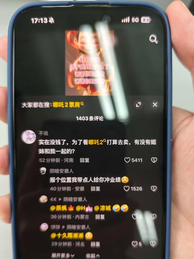 这是一张抖音竖屏截图，顶部是《哪吒之魔童闹海》（哪吒2）的哪吒庆祝图，配文“好开心哦 终于跑到第六名了 谢谢你的点赞 谢谢你的支持”，对应影片票房跻身影史第六的热点消息。下方评论区中，用户“不说”用夸张玩梗的方式发言：“实在没钱了，为了看哪吒2打算去卖，有没有姐妹和我一起的？”，用户“阴暗安徽人”随即接梗回复：“报个位置我带点人给你冲业绩”，后续还有其他用户的@互动内容。整体是网友围绕热门电影《哪吒2》展开的趣味调侃，用夸张的玩笑表达对影片的期待与喜爱，其中“卖”是纯粹的玩梗，无不良含义，属于夸张式的调侃。
